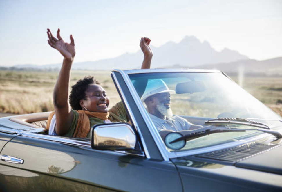 A happy retired couple driving to the mountains in their convertible car.