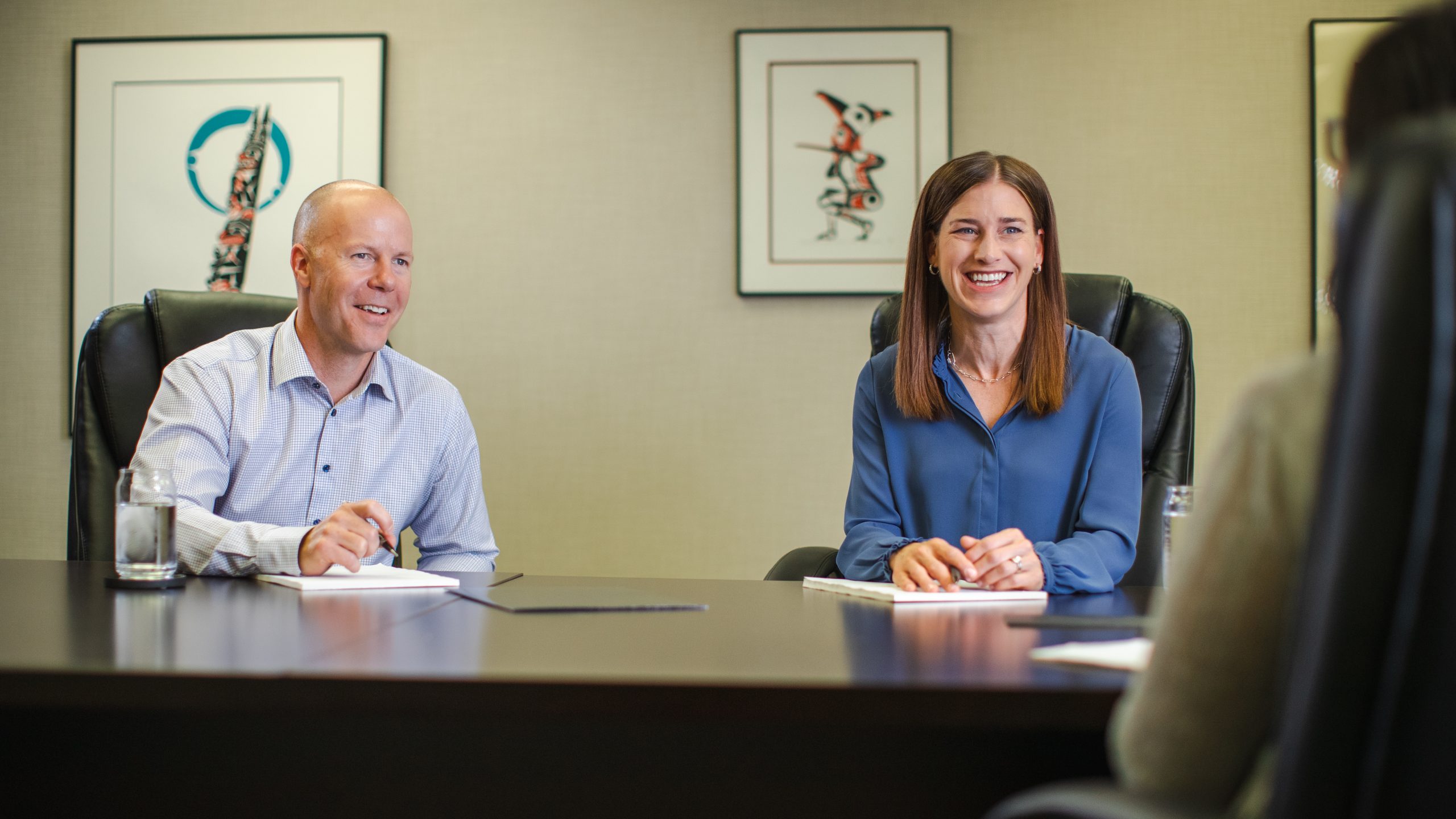 Two Financial Planners sitting at a boardroom table laughing with a client.