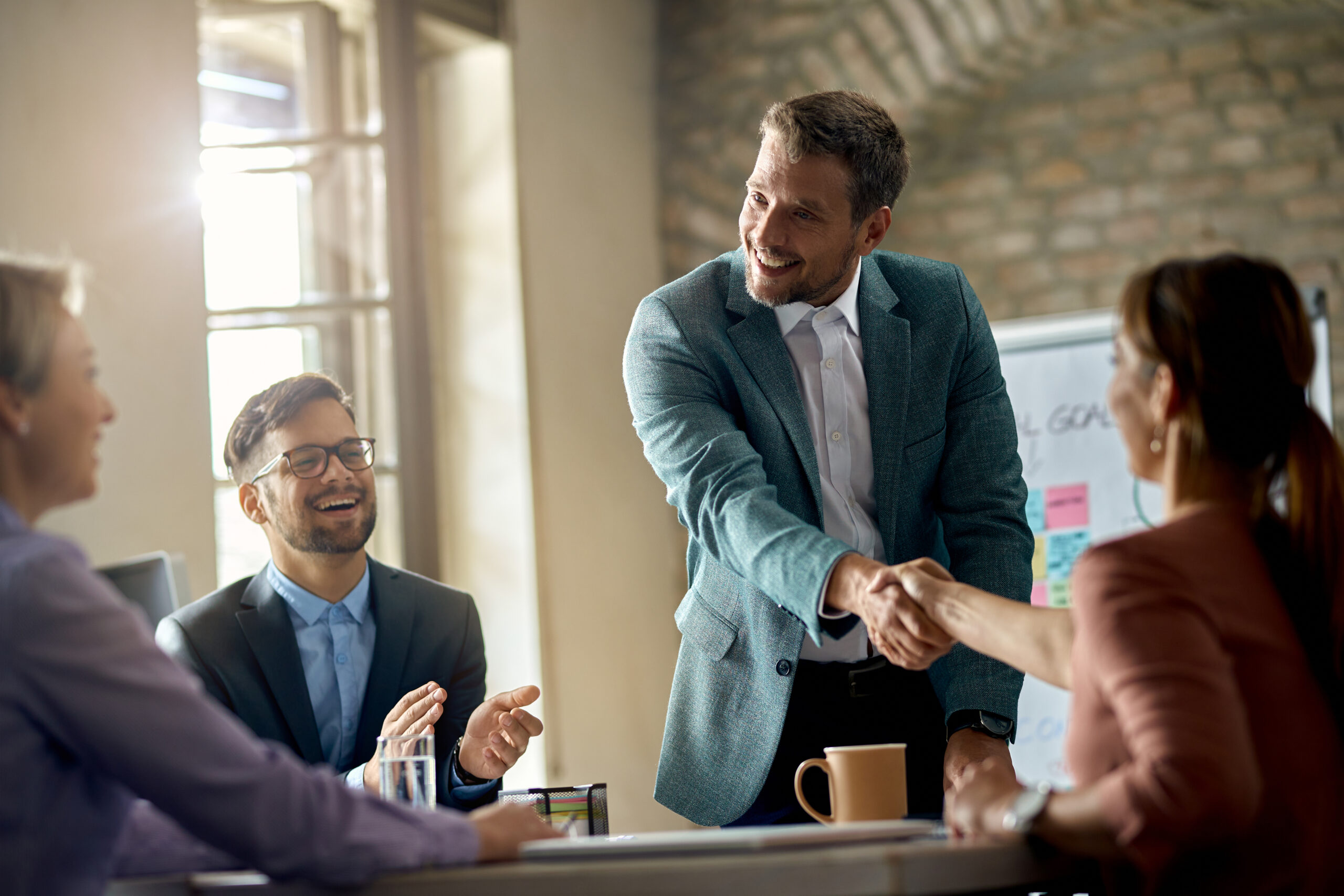 Happy business partners greeting their colleagues in a meeting and shaking hands with one of them in the office. Image by Drazen Zigic on Freepik